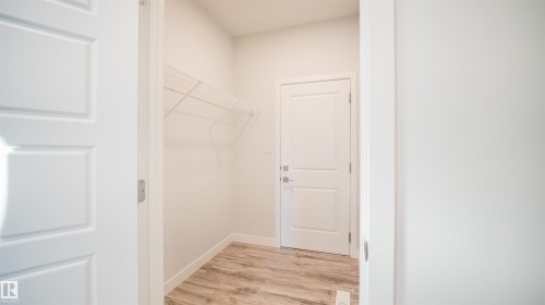 Utility room featuring a paneled door, wood-finish flooring, white baseboards, and wire shelving - 44 Dalquist Bay, Leduc, AB 