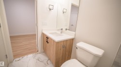 Bathroom featuring a wood-finish vanity with a white countertop and integrated sink, chrome faucet, and rectangular wall-mounted mirror - 