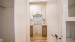 Compact kitchen area featuring wood-finish flooring, white upper cabinetry, and a stainless steel range hood - 