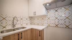 Modern kitchen featuring a dual basin stainless steel sink, a chrome pull-down faucet, and light wood-finish lower cabinetry with matte black hardware - 