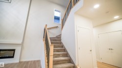 Vaulted ceiling with an upper window, contemporary fireplace, carpeted staircase with wood and metal railing, recessed lighting, and wood-finish flooring - 