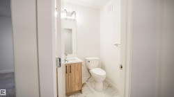 Powder room featuring a white pedestal toilet, wood-finish vanity with a white countertop and rectangular sink, and patterned floor tile - 