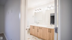 Bathroom featuring a dual vanity with wood-finish cabinetry, white countertop, two undermount sinks, and separate mirrors with overhead light fixtures - 