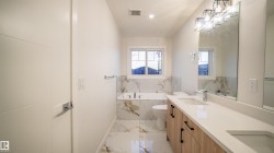 Modern bathroom featuring a double vanity with light wood-finish cabinetry and white countertops - 