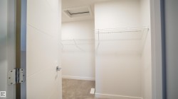 Walk-in closet featuring white wire shelving, light-toned carpeting, white baseboards, and a white ceiling with an access panel - 