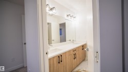 Bathroom vanity featuring a light wood-finish double-sink cabinet, white countertops, and contemporary black hardware - 