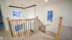 Two-story staircase featuring light wood railings with black metal balusters, carpeted treads, and a contemporary geometric chandelier - 