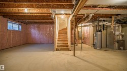 Unfinished basement featuring exposed wood joists, concrete flooring, and a visible staircase - 