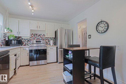 Kitchen featuring white cabinetry, a colorful mosaic tile backsplash, stainless steel appliances, and wood-finish flooring - 2007 67 Street, Edmonton, AB 