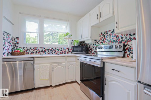Bright kitchen featuring white cabinetry, a colorful mosaic tile backsplash, stainless steel dishwasher, and a freestanding range with a flat cooktop - 2007 67 Street, Edmonton, AB 