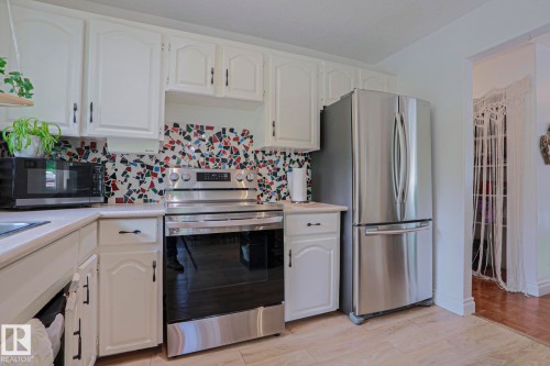 Kitchen featuring white cabinetry and a multicolor mosaic tile backsplash - 2007 67 Street, Edmonton, AB 