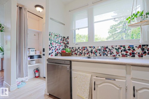 Kitchen area with a stainless steel dishwasher, mosaic tile backsplash, and a double-basin sink under a large window - 2007 67 Street, Edmonton, AB 