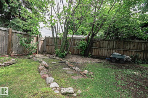 Fenced backyard featuring mature trees, a stone-lined pathway, and stepping stones - 2007 67 Street, Edmonton, AB 