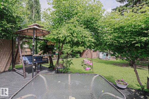 Expansive backyard featuring a lush lawn, mature trees, and a dark-toned deck - 2007 67 Street, Edmonton, AB 