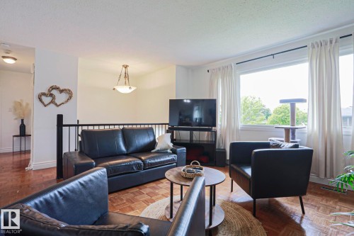 Open-concept living area featuring wood-finish flooring, a prominent window, a ceiling-mounted light fixture, and a black metal railing - 2007 67 Street, Edmonton, AB 