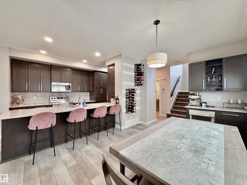 Kitchen featuring wood-finish flooring, dark cabinetry, light-toned countertops, and stainless steel appliances - 302 Balsam Link, Leduc, AB 