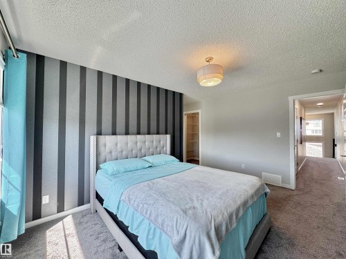 Carpeted bedroom featuring a striped accent wall, light gray painted walls, recessed built-in shelving, and a drum-style ceiling light fixture - 302 Balsam Link, Leduc, AB 