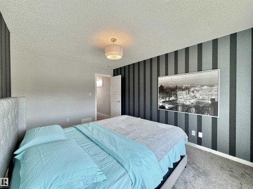 Bedroom featuring textured striped accent wall, light gray painted walls, and gray carpeted flooring - 302 Balsam Link, Leduc, AB 