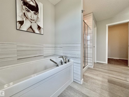 Soaking tub with polished chrome fixtures, white subway tile surround, glass-enclosed shower, wood-finish flooring, and light gray wall paint - 302 Balsam Link, Leduc, AB 