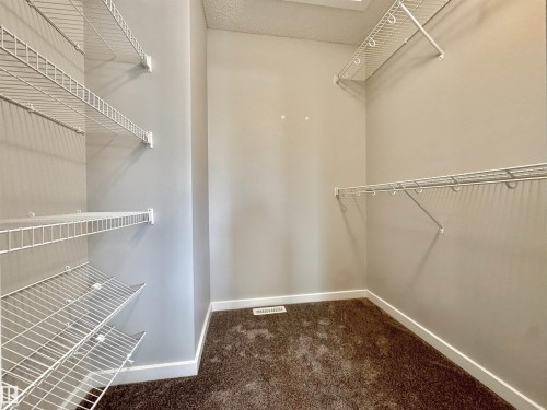 Walk-in closet featuring wire shelving, wire hanging rods, neutral wall paint, white baseboards, and brown carpeting - 302 Balsam Link, Leduc, AB 