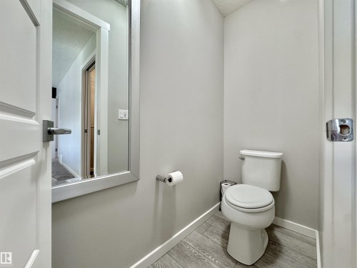 Powder room featuring light gray walls, wood-finish flooring, white baseboards, and a contemporary mirror - 302 Balsam Link, Leduc, AB 