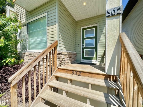 Exterior featuring light green horizontal siding, a stone veneer foundation, and a prominent green entry door with three rectangular lites - 302 Balsam Link, Leduc, AB 