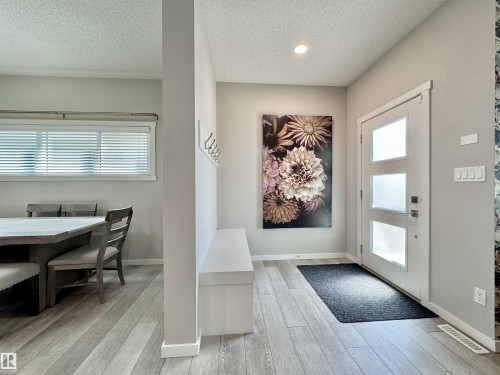 Entryway featuring a modern front door with three frosted glass panels, wood-finish flooring, and a built-in bench with coat hooks - 302 Balsam Link, Leduc, AB 