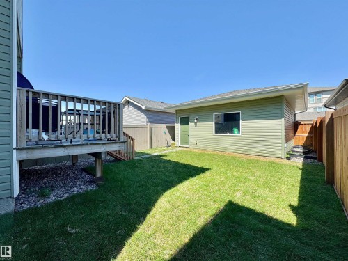 Expansive backyard featuring a wood deck with railings, a manicured lawn, a detached utility building with a window and door, and privacy fencing - 302 Balsam Link, Leduc, AB 