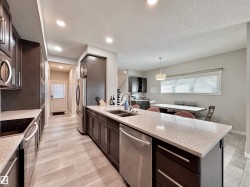 Kitchen featuring wood-finish flooring, dark wood cabinetry, light-toned countertops, stainless steel appliances, and recessed lighting - 