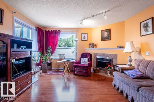 A bright Living area featuring laminate flooring, a corner fireplace with a tiled surround, access to the covered balcony. - 303 10528 77 Avenue, Edmonton, AB 