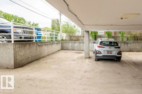 Partially Covered parking space featuring concrete flooring, a concrete support column, and an overhead light fixture - 303 10528 77 Avenue, Edmonton, AB 