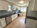 Contemporary kitchen featuring white cabinetry, dark granite countertops, and a gray mosaic tile backsplash - 12010 66 Street, Edmonton, AB 