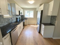 Modern kitchen featuring white cabinetry, dark countertops, full tile backsplash, stainless steel appliances, and light wood-finish flooring - 