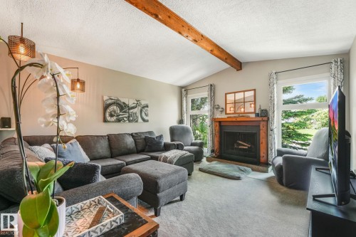 Vaulted ceiling with an exposed wood beam, a wood-surround fireplace with a black insert, and two large windows offering natural light - 17237 104 Street, Edmonton, AB 