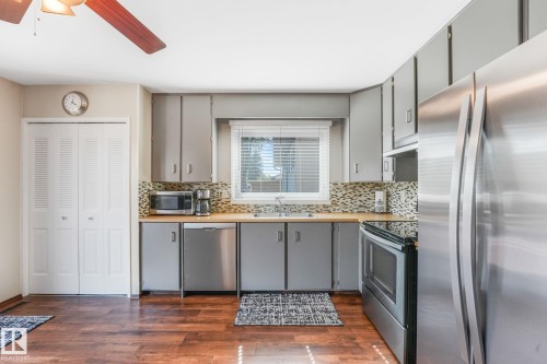 Kitchen featuring wood-finish flooring, gray cabinetry, stainless steel appliances, and a mosaic tile backsplash - 17237 104 Street, Edmonton, AB 