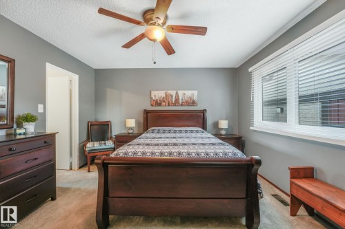 Spacious bedroom featuring neutral wall tones, textured ceiling, a ceiling fan with integrated lighting, a large window with blinds, and carpeted flooring - 17237 104 Street, Edmonton, AB 