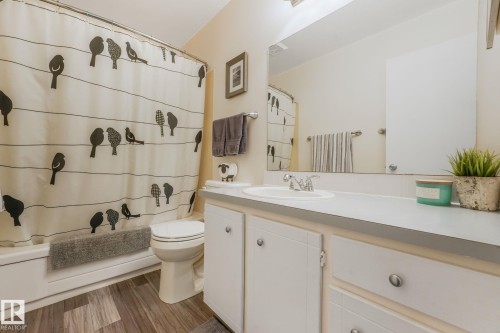 Bathroom featuring a white vanity with integrated sink, a full-width mirror, a white bathtub with a shower, and wood-finish flooring - 17237 104 Street, Edmonton, AB 