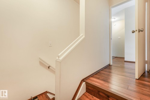 Staircase featuring wood-finish flooring, a white painted handrail, and light neutral wall finishes - 17237 104 Street, Edmonton, AB 