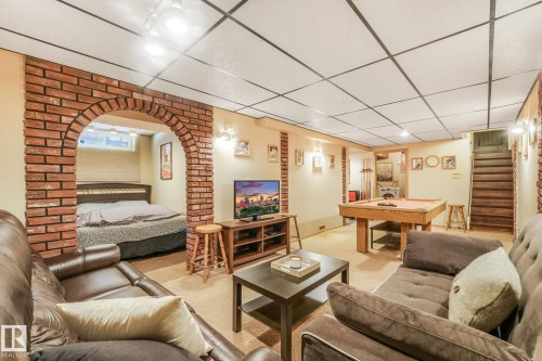 Lower-level recreational space featuring an exposed brick archway, recessed lighting, drop ceiling, carpeted flooring, and a visible staircase - 17237 104 Street, Edmonton, AB 