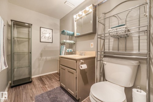 Bathroom featuring wood-finish flooring, a vanity with a light-colored countertop and cabinetry, a mirrored medicine cabinet with integrated lighting, and a chrome-finish over-the-toilet storage unit - 17237 104 Street, Edmonton, AB 