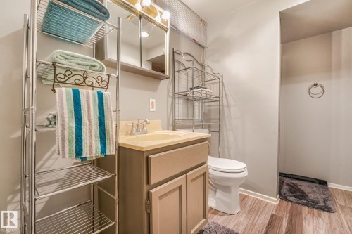 Bathroom featuring wood-finish flooring, a vanity with a light-toned countertop, a wall-mounted mirror with integrated lighting, a toilet, and a shower area with a dark-toned floor - 17237 104 Street, Edmonton, AB 