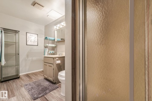 Bathroom featuring a single vanity, wood-finish flooring, and a glass-front shower enclosure - 17237 104 Street, Edmonton, AB 