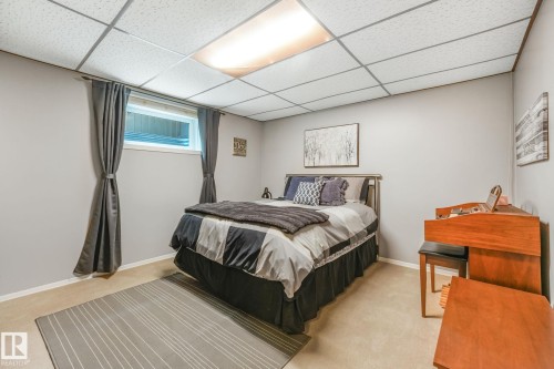 Spacious bedroom featuring light gray painted walls, a large horizontal window with gray curtains, neutral carpet flooring, and a drop ceiling with integrated lighting - 17237 104 Street, Edmonton, AB 