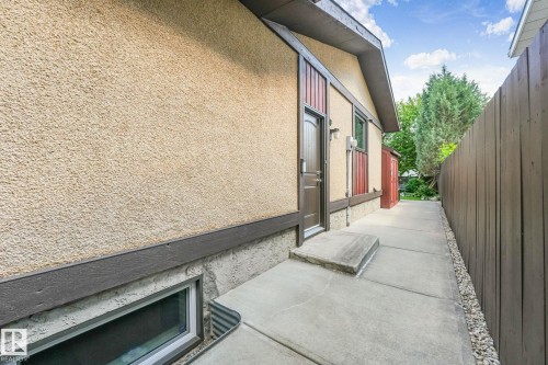 Stucco exterior with concrete walkway, brown privacy fencing, and a built-in window well - 17237 104 Street, Edmonton, AB 