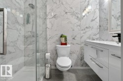 Contemporary bathroom featuring large format marble-look wall tiles, a frameless glass shower enclosure, a white floating vanity with integrated sink, and dark gray tile flooring - 
