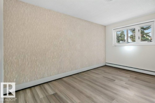 Room featuring wood-finish flooring, white baseboards, and a textured accent wall - 6916 92A Avenue, Edmonton, AB 