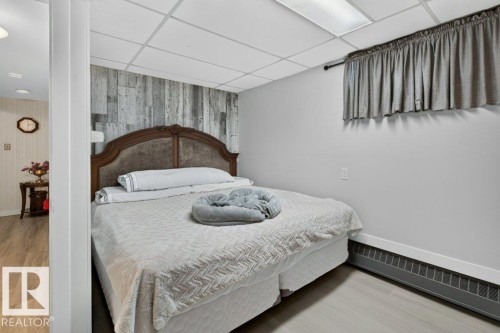 Bedroom featuring a decorative wood-finish accent wall, light grey walls, and light wood-look flooring - 6916 92A Avenue, Edmonton, AB 