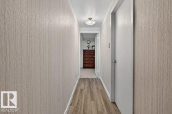 Hallway featuring wood-finish flooring, textured wall coverings, a ceiling-mounted light fixture, and white interior doors with round knobs - 
