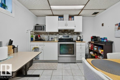 Kitchen featuring white cabinetry, stainless steel range, and mosaic tile backsplash - 6916 92A Avenue, Edmonton, AB 