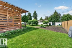 Expansive backyard featuring a manicured lawn, a raised garden bed, and a slatted wood privacy structure with a translucent roof - 